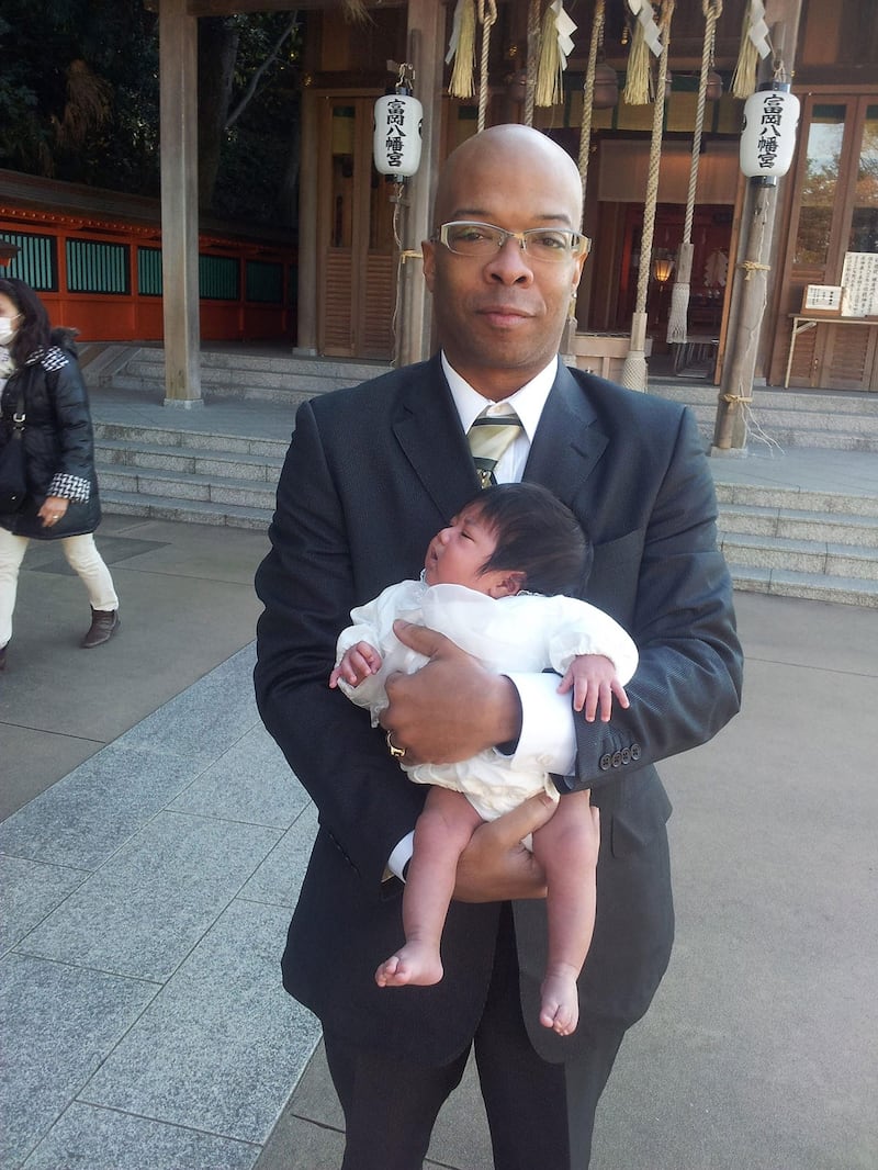 2013年，小威尔斯与刚出生不久的女儿贾丝明在日本横滨的一座神社前合影。（威尔斯一家提供）